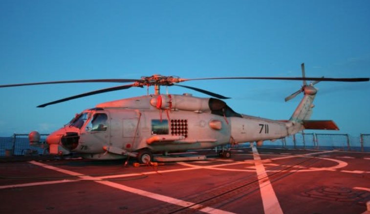 A Navy SH-60B Seahawk helicopter, number 711, on a ship's flight deck at sunset