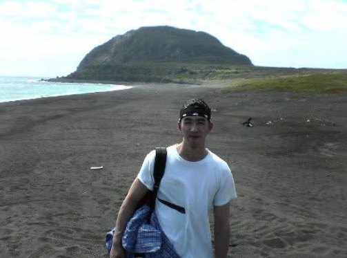 Norman Wong on the black sand beach at Iwo Jima, with Mount Suribachi behind him