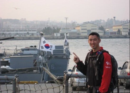 Norman Wong at a harbor in South Korea, beside a South Korean flag